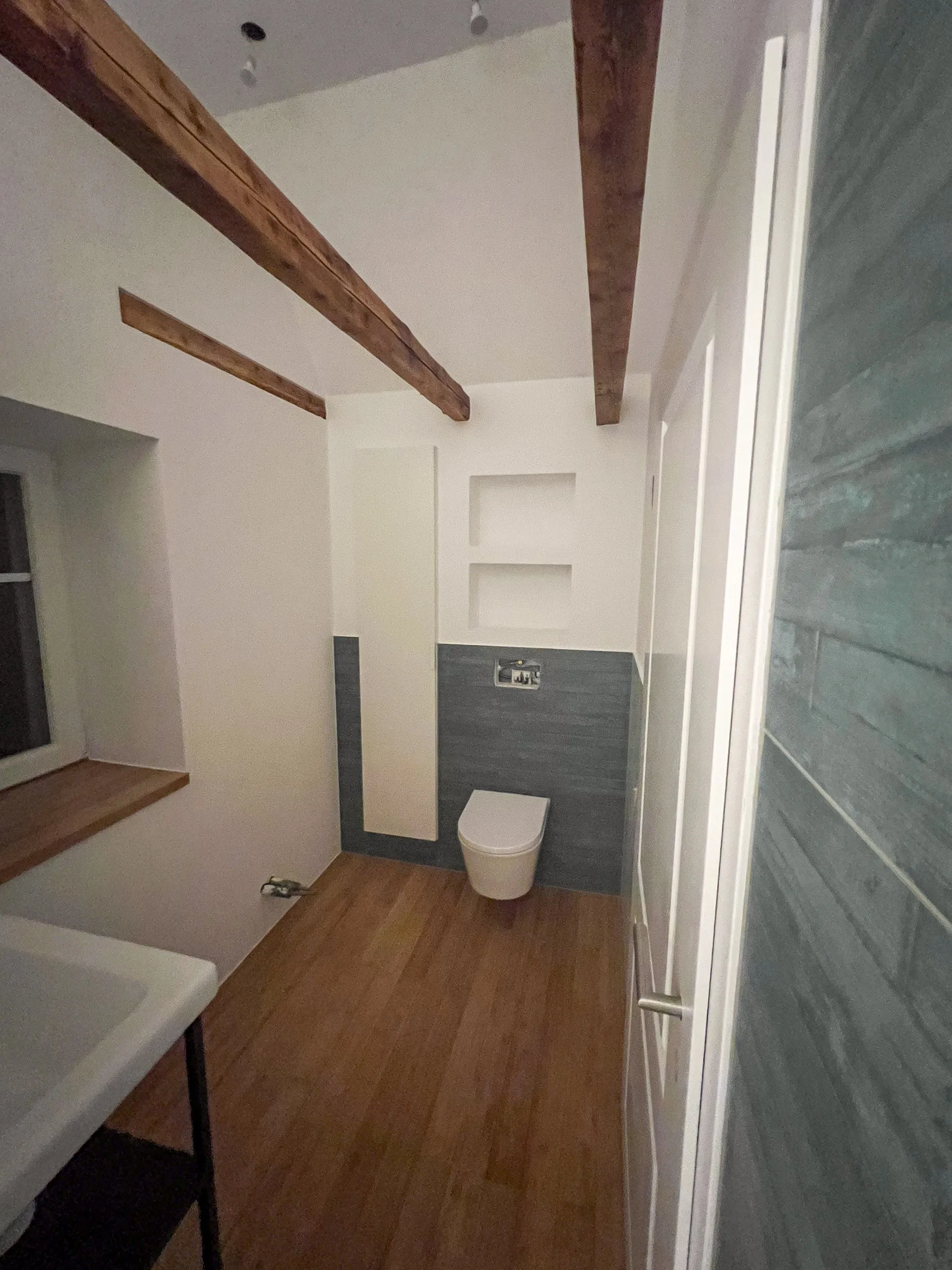 Modernisiertes Badezimmer mit sichtbaren Holzbalken, blauen Wandfliesen, Nischen und wandhängendem WC – Altbausanierung durch Trockenbau Plus in Coesfeld