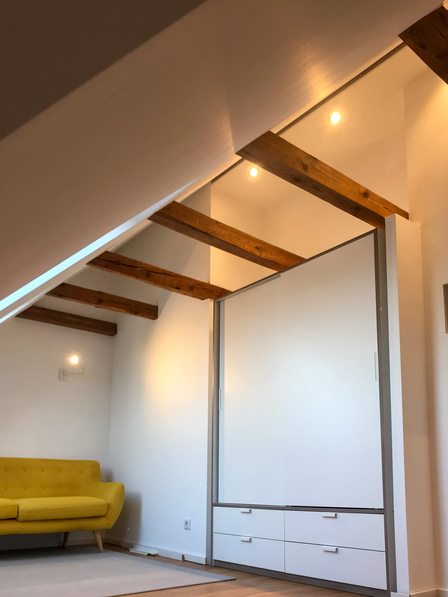 Modernisierter Wohnraum mit sichtbaren Holzbalken, Einbauschrank und gelbem Sofa – Altbausanierung durch Trockenbau Plus in Coesfeld