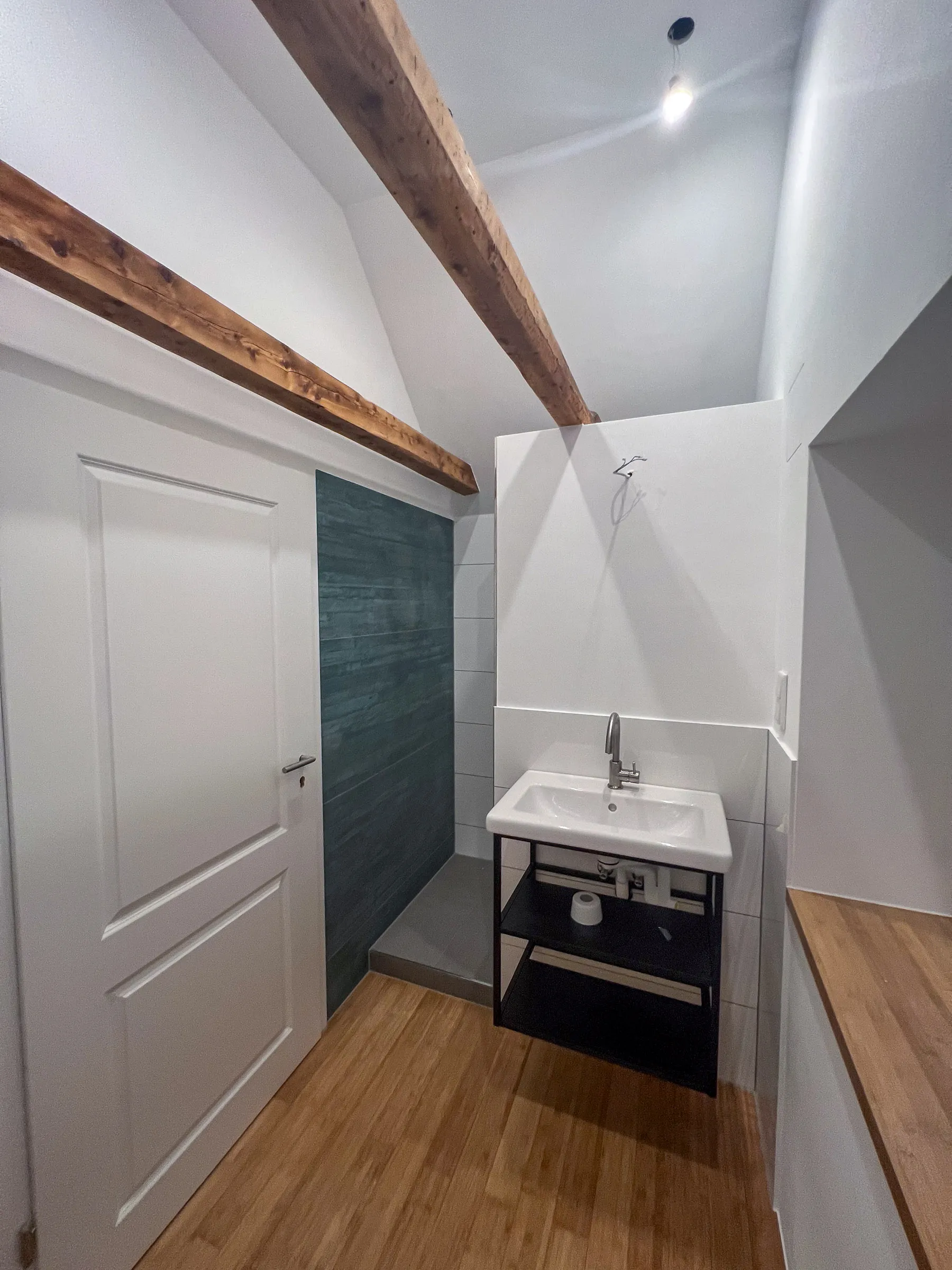 Modernisiertes Bad mit sichtbaren Holzbalken, offenem Waschtisch und begehbarer Dusche mit strukturierter Wandfliese – umgesetzt von Trockenbau Plus in Coesfeld